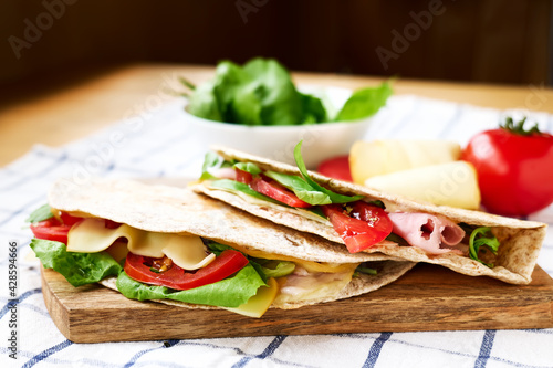 Piadina Romagnola with mozzarella cheese, tomatoes, ham and rocket salad on a cutting board on the table. Italian flatbread or open sandwich. Selective focus.
