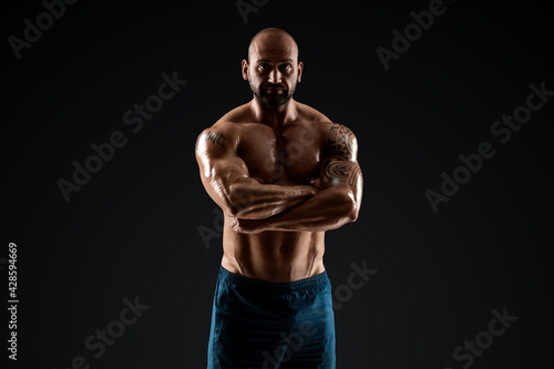 Tattooed male bodybuilder posing over black background. Fitness workout concept, muscle groups, watch your body.