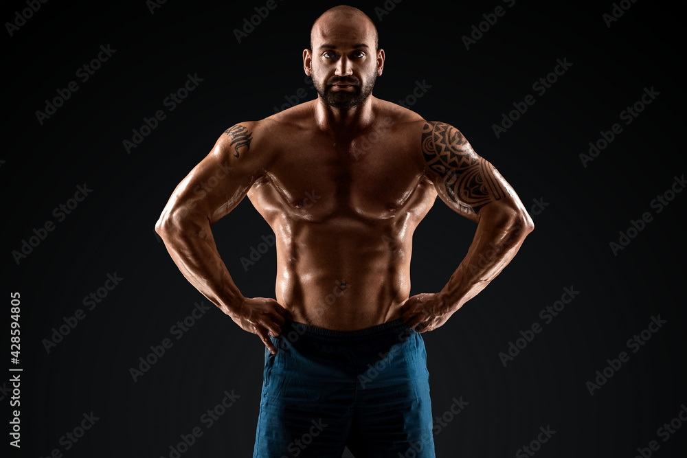 Fototapeta premium Tattooed male bodybuilder posing over black background. Fitness workout concept, muscle groups, watch your body.