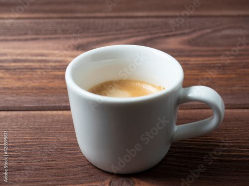 a white cup with a delicious and aromatic espresso on a wooden background. side view