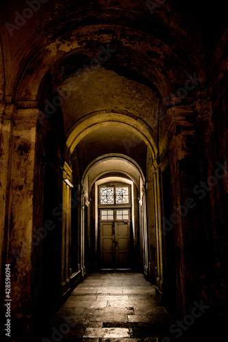 A gloomy corridor with a door at the end, from which comes the light.