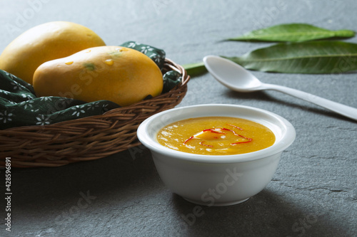 Aamras is plain Haapus or Alphonso Mango Puree/Pulp with kesar/ saffron topping. Aam Ras is a delicious Indian seasonal Dessert recipe. Served in a white bowl with mangos and puri or poori. photo