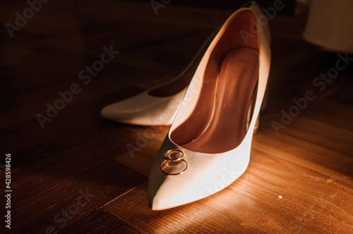 White shoes of the bride and a pair of gold wedding rings on a brown background. Wedding accessories