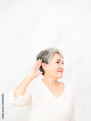 Senior asian woman smiling with hand over ear listening an hearing to rumor or gossip in white background.