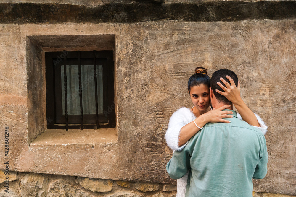 a couple embracing on the wall of an old house. the girl looks in a sensual way.