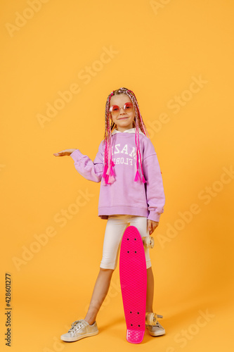 Active young girl in pink shirt and white shorts holding skatebo