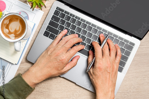 Man's hand typing laptop computer and notebook, coffee on wooden table