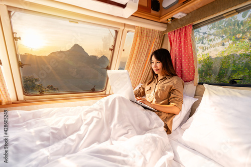 Young woman traveler laying in camper van and using laptop to watch movies and listen to music while road trip traveling on vacation