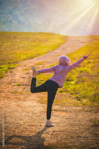 Young woman wearing a training clothes. She is stretching her leg and arms ready to workout in the morning. Young woman warming up outdoor with sunlight in the morning.
