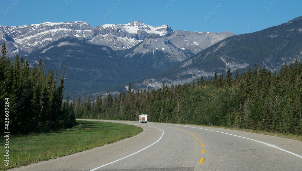 Fototapeta premium driving down a lonely road to the mountains with a forest on each side
