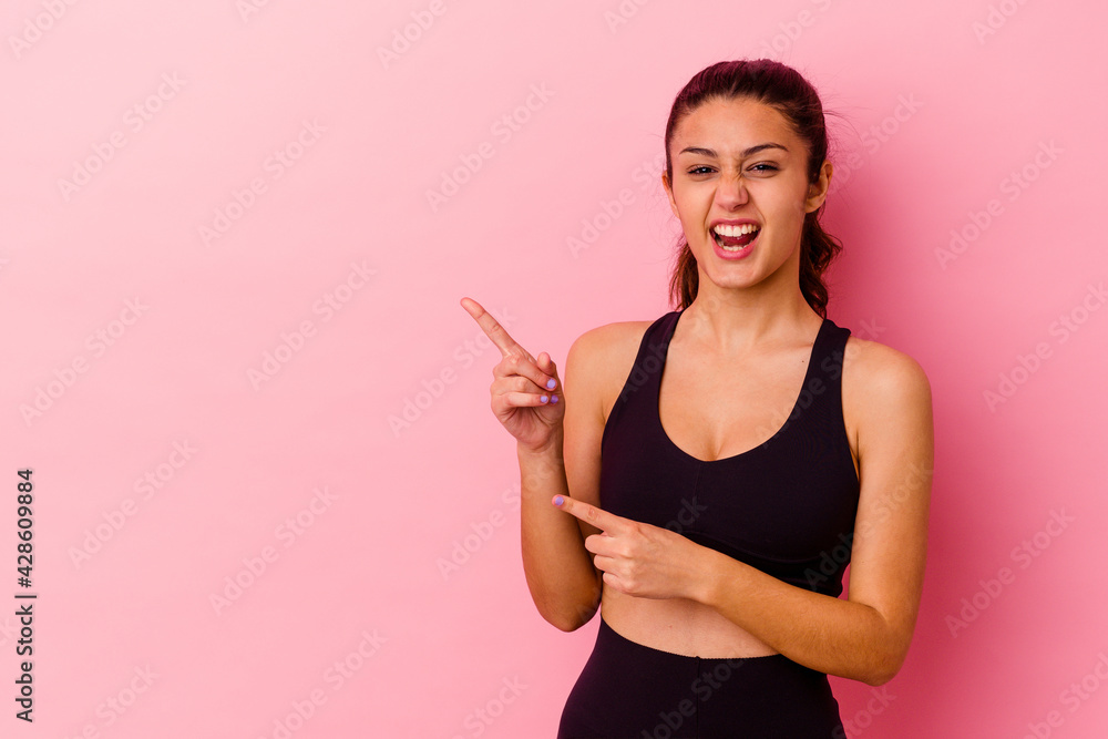 Young sport Indian woman isolated on pink background pointing with forefingers to a copy space, expressing excitement and desire. Young sport Indian woman isolated on pink background pointing with forefingers to a copy space, expressing excitement and desire.