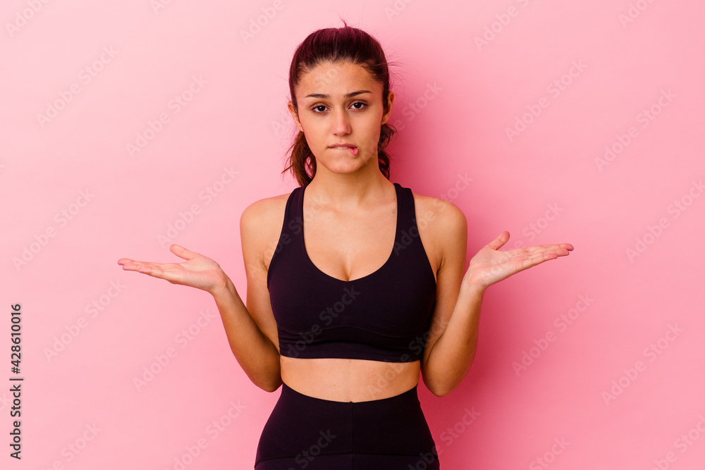 Young sport Indian woman isolated on pink background confused and doubtful shrugging shoulders to hold a copy space. Young sport Indian woman isolated on pink background confused and doubtful shrugging shoulders to hold a copy space.