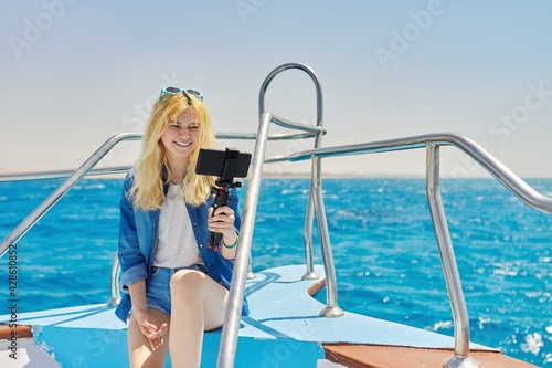 Young woman recording stream on smartphone sitting on board of yacht in sea © Valerii Honcharuk