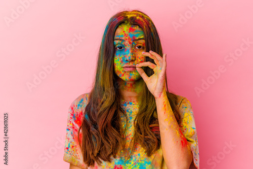 Young Indian woman celebrating holy festival isolated on white background with fingers on lips keeping a secret.