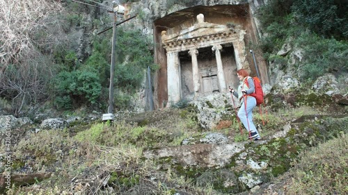 Redhead Caucasian woman walks downhill using trekking poles after visiting Amynthas Rock Tomb in Fethiye, Turkey. photo