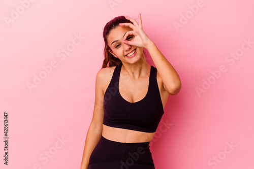 Young sport Indian woman isolated on pink background excited keeping ok gesture on eye. © Asier