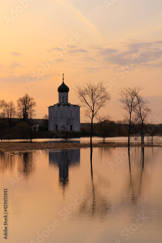 Watercolor dawn landscape in high water - with the silhouette of a church and reflections on the surface of a meadow flooded with melting snow. © Irina Solonina