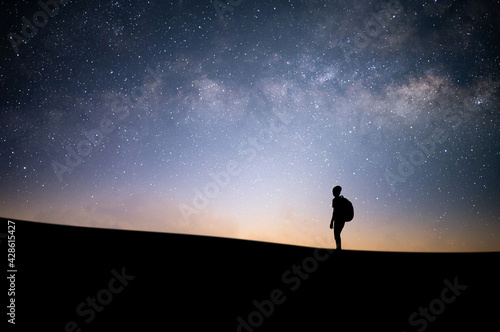 Silhouette of young traveler and backpacker watched the beautiful night sky, star and milky way alone on top of the mountain. He enjoyed traveling and was successful when he reached the summit.