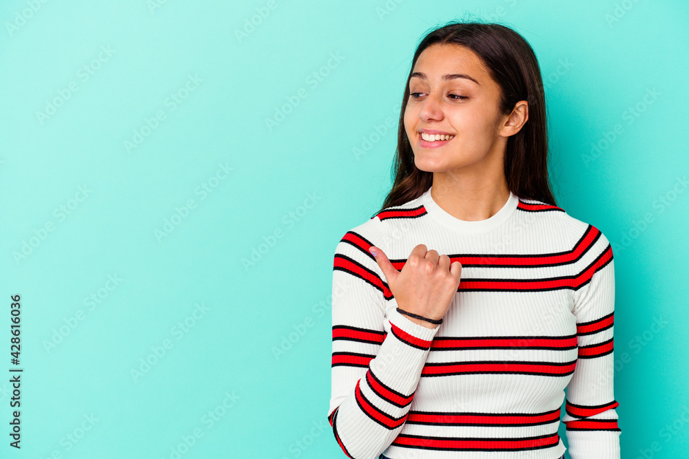 Young Indian woman isolated on blue background points with thumb finger away, laughing and carefree. Young Indian woman isolated on blue background points with thumb finger away, laughing and carefree.