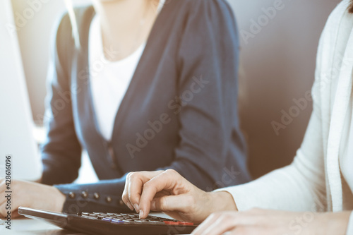 Accountant checking financial statement or counting by calculator income for tax form, hands closeup. Business woman sitting and working with colleague at the desk in office. Tax and Audit concept