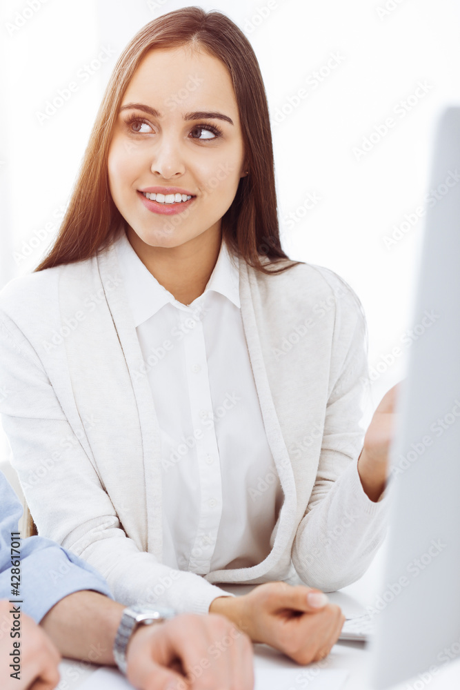 Young woman sitting at the desk with computer in sunny office. Looks like student girl or business lady communicating with casual dressed man Young woman sitting at the desk with computer in sunny office. Looks like student girl or business lady communicating with casual dressed man