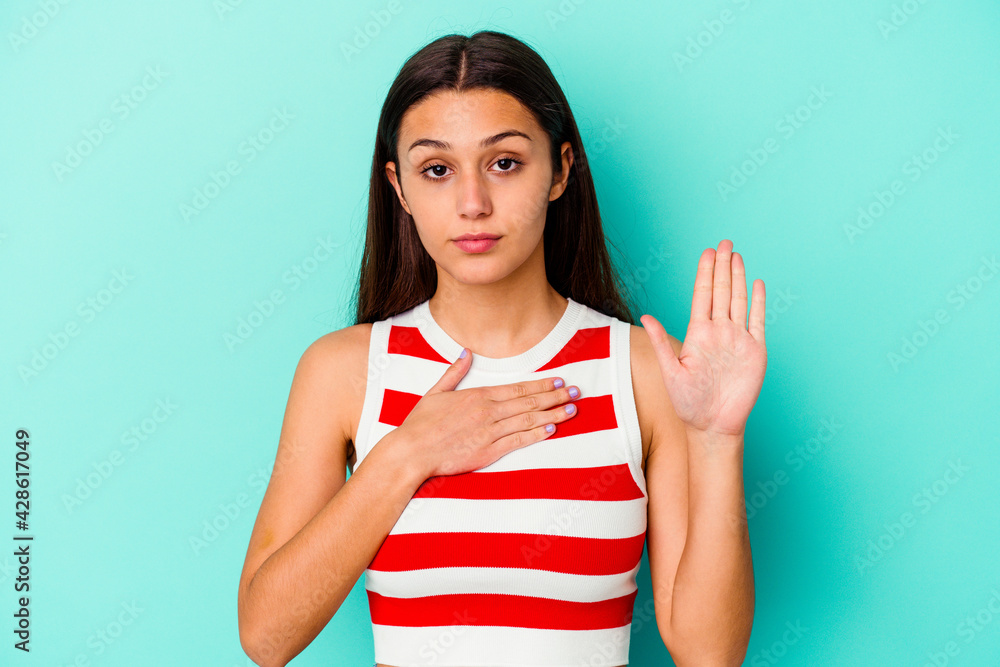 Young Indian woman isolated on blue background taking an oath, putting hand on chest. Young Indian woman isolated on blue background taking an oath, putting hand on chest.