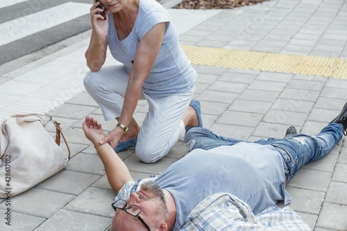Senior passerby kneels beside the person who fainted on the street and calls an ambulance