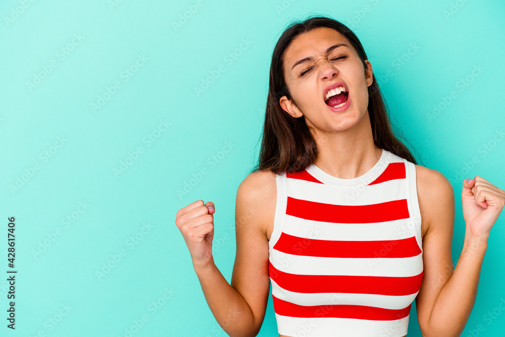 Young Indian woman isolated on blue background raising fist after a victory, winner concept. Young Indian woman isolated on blue background raising fist after a victory, winner concept.