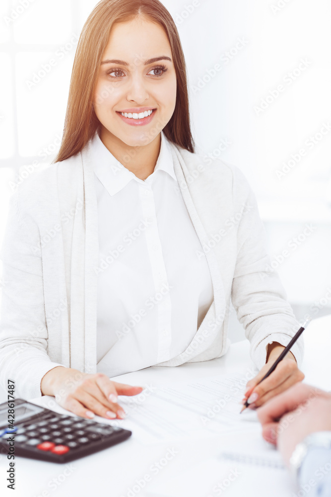 Young business woman and man sitting and working with computer and calculator in sunny office. Tax and audit concepts