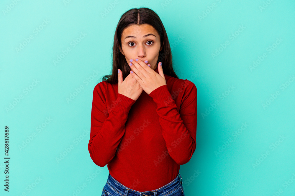 Young Indian woman isolated on blue background shocked covering mouth with hands. Young Indian woman isolated on blue background shocked covering mouth with hands.