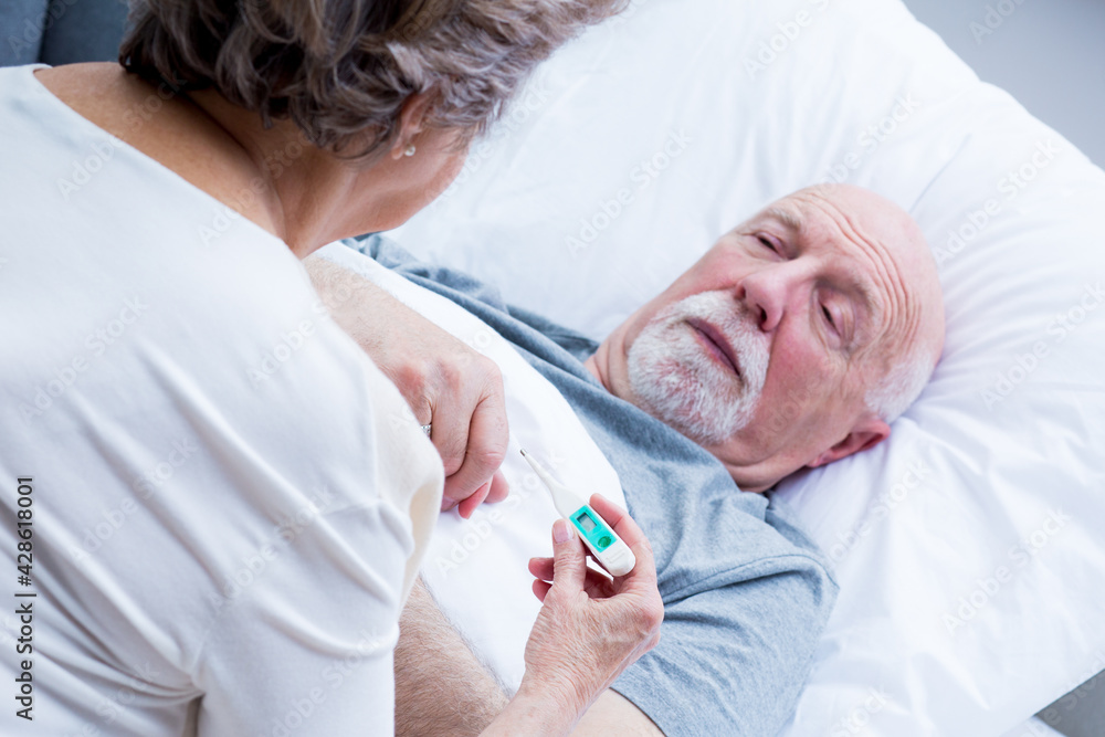 Elderly wife measures the temperature of her sick husband lying in bed Elderly wife measures the temperature of her sick husband lying in bed