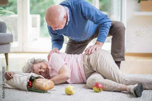 Foto Senior woman lying on the floor of her apartment, and her husband helping her to
