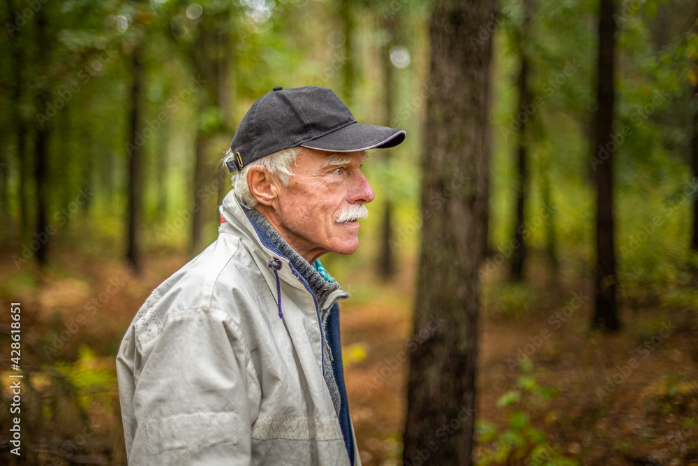 A mature man wearing a cap walking in the woods during the day. A mature man wearing a cap walking in the woods during the day.