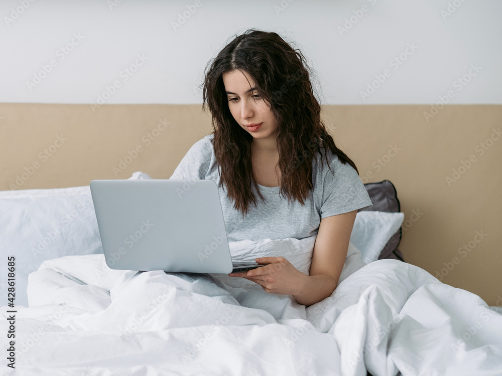 Gadget morning. Remote work. Online job. Freelancer lifestyle. Relaxed confident woman using laptop in white bed in light bedroom home office. Gadget morning. Remote work. Online job. Freelancer lifestyle. Relaxed confident woman using laptop in white bed in light bedroom home office.
