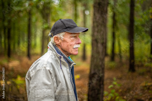 A mature man wearing a cap walking in the woods during the day.