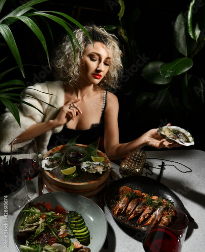 Canvastavla Rich wealthy woman in black dress has a dinner in seafood restaurant sits holdin