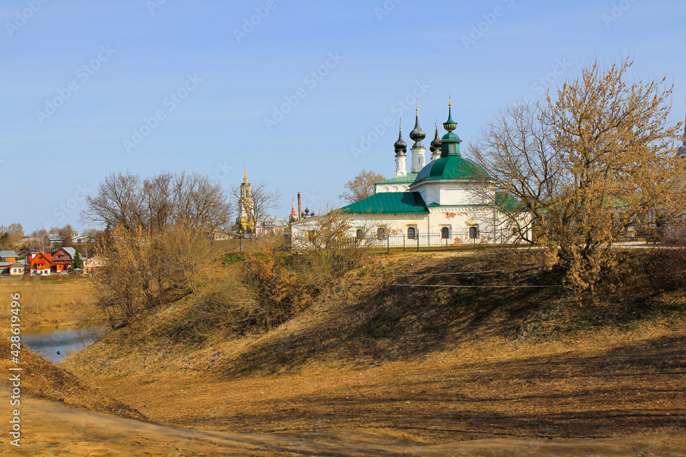 The Church of Paraskeva Pyatnitsa in Suzdal stands on a hill on the banks of the Kamenka River, surrounded by trees - on a clear April day.