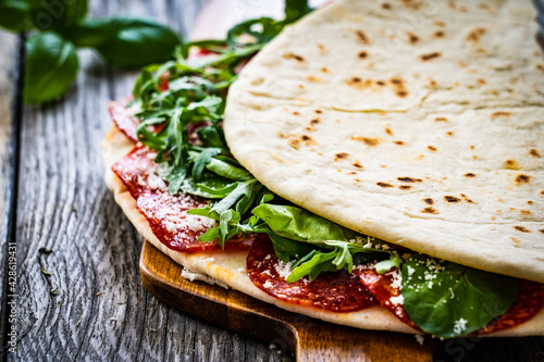 Italian piada wraps - piadina stuffed with fresh vegetable leaves and salami sausage on wooden table
