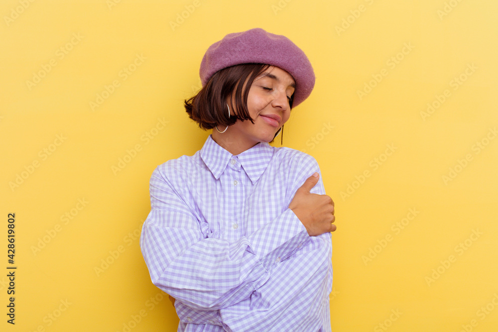 Young mixed race woman wearing a beret isolated on yellow background hugs, smiling carefree and happy. Young mixed race woman wearing a beret isolated on yellow background hugs, smiling carefree and happy.