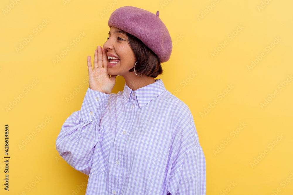 Young mixed race woman wearing a beret isolated on yellow background shouting and holding palm near opened mouth. Young mixed race woman wearing a beret isolated on yellow background shouting and holding palm near opened mouth.
