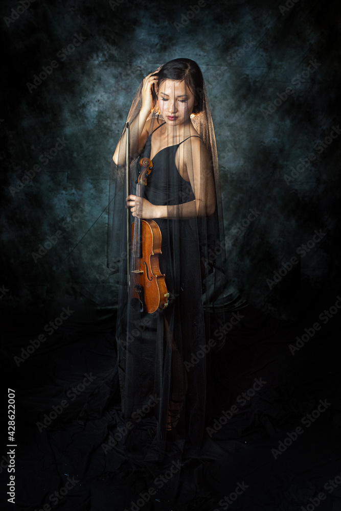 Young Asian Woman is holding a violin. She is covered with a veil und standing on the stage.  Violin Concert. Performance.  Violinist