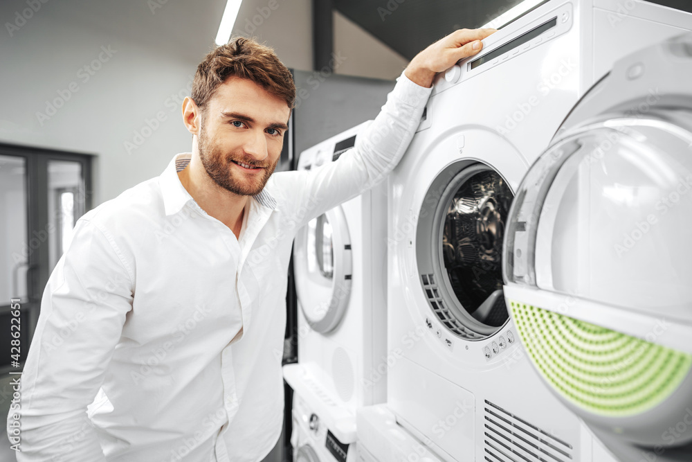 Young man choosing new washing machine in household appliances store Young man choosing new washing machine in household appliances store