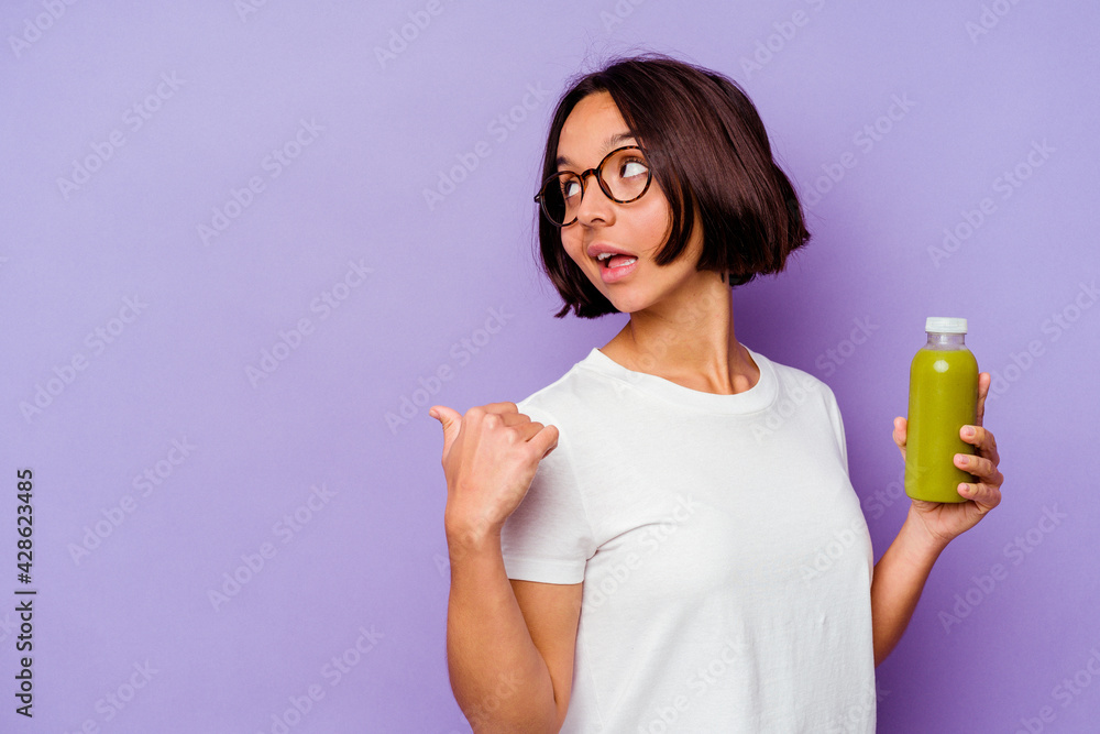 Young mixed race woman holding a healthy smoothie isolated on purple background points with thumb finger away, laughing and carefree. Young mixed race woman holding a healthy smoothie isolated on purple background points with thumb finger away, laughing and carefree.