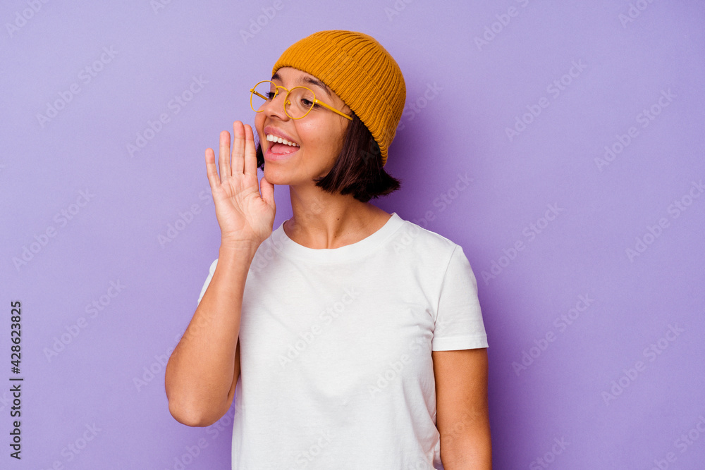 Young mixed race woman wearing a wool cap isolated on purple background shouting and holding palm near opened mouth. Young mixed race woman wearing a wool cap isolated on purple background shouting and holding palm near opened mouth.