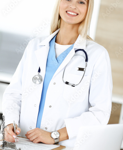 Woman-doctor at work in clinic happy of her profession. Blond female physician controls medication history record and medical exam results. Medicine concept