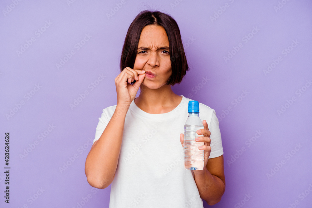 Young mixed race holding a water bottle isolated on purple background with fingers on lips keeping a secret. Young mixed race holding a water bottle isolated on purple background with fingers on lips keeping a secret.
