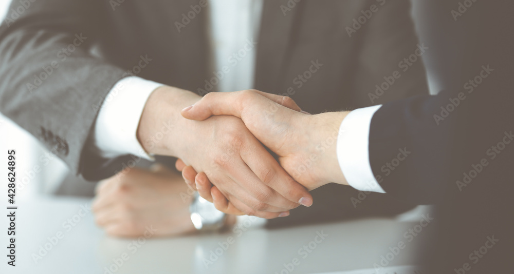 Unknown businessman shaking hands with his colleague or partner above the glass desk in modern office, close-up. Business people group at meeting Unknown businessman shaking hands with his colleague or partner above the glass desk in modern office, close-up. Business people group at meeting