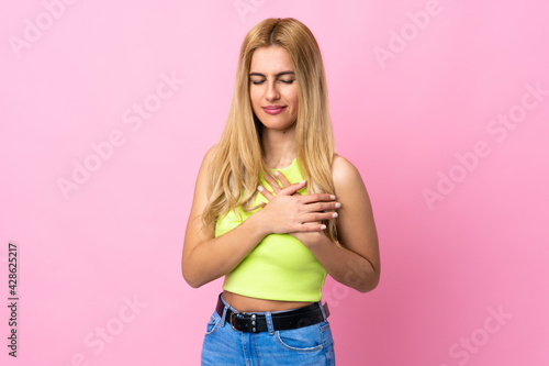Young Uruguayan blonde woman over isolated pink background having a pain in the heart