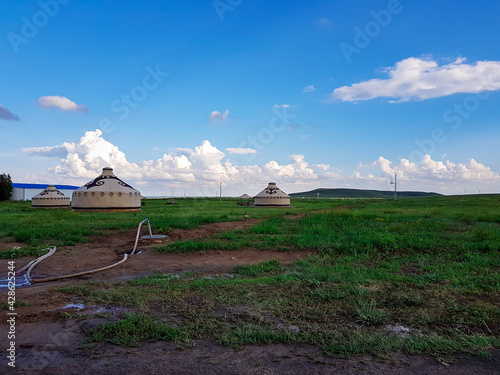 A few white, traditional yurts located on a pasture in Xilinhot in Inner Mongolia. Endless grassland. Blue sky with a few thick, white clouds. A long garden hose in front. Nomadic way of life. photo