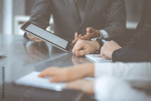 Unknown businessman using tablet computer and working together with his colleague while sits at the glass desk in modern office. Teamwork and partnership concept